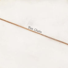 A 18K gold box chain necklace laid diagonally across a white background, with the text 'Box Chain' printed near the center.