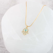 Close up view of 18K gold plated hamsa hand evil eye pendant necklace on a stone jewelry tray. 