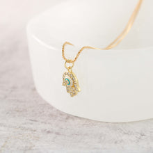 Side view of gold plated hamsa hand evil eye necklace in a jewelry tray. 