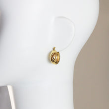 A small gold hoop earring with a textured, openwork design displayed on a white mannequin head against a neutral beige background.