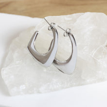 Contoured silver drop earrings stainless steel on crystal stone jewelry display. 