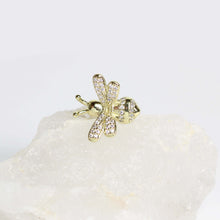 A close-up of a person's ear showcasing a gold bee-shaped ear cuff adorned with small clear crystals, alongside other gold hoop and stud earrings.