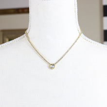 A gold-tone stainless steel necklace with a heart-shaped pendant featuring a rhinestone on a mannequin. 