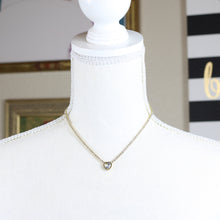 A gold-tone stainless steel necklace with a heart-shaped pendant featuring a rhinestone on a mannequin. 