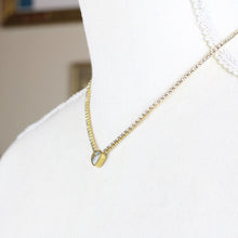 Close up view of a gold-tone stainless steel necklace with a heart-shaped pendant featuring a rhinestone on a mannequin. 