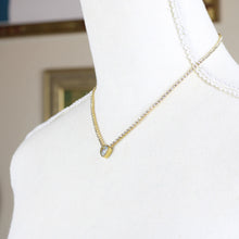 Close up view of a gold-tone stainless steel necklace with a heart-shaped pendant featuring a rhinestone on a mannequin. 