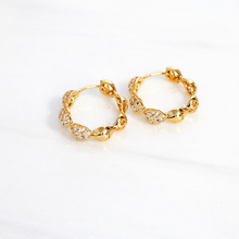 A pair of gold huggie hoop earrings with textured, twisted links and pavé-set clear stones, displayed on a clean white surface.