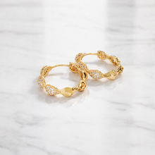 A pair of gold hoop earrings with pavé-set clear stones and textured organic links, displayed on a white marble surface.
