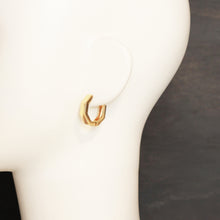 A gold geometric hoop earring displayed on a white mannequin head against a dark gray background.
