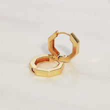 A pair of gold geometric hoop earrings with a faceted, stepped octagonal design, displayed on a clean white surface.