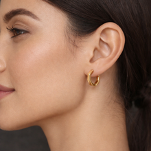 A close-up side profile of a woman wearing a small gold hoop earring with a textured, geometric open design.