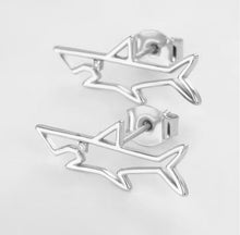 Close up of shark stud earrings on light grey background. 