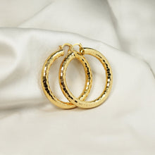 Close-up of 18K gold plated hoop earrings showing light-reflecting faceted pattern and secure hinge closure