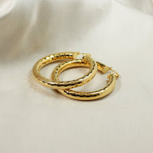Close-up of 18K gold plated hoop earrings showing light-reflecting faceted pattern and secure hinge closure