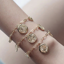 A gold charm bracelet with three charms, displayed on a wrist.